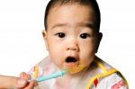 Close Up Of Happy Little Seven Months Old Son In See Through Plastic Bib Eating In Chair For Babies After Mom Made Him Eat Avocado And Banana Mix.happy Baby's Face. Asian Infant Open Mouth Stock Photo