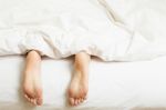 Woman's Feet Sticking Out Of Blanket On Bed At Home Stock Photo