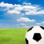 Soccer Ball With Green Grass Field Against Blue Sky Stock Photo