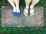 Top View Feet Of Male And Female Couple Lover Standing On Stone Floor Among Little Green Grass Garden. Hipster Style Stock Photo