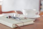 Notebook With Pen, Eyeglasses And White Coffee Cup Stock Photo