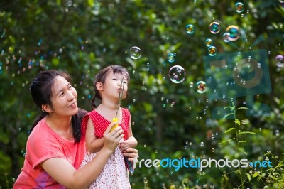 Asian Lovely Girl And Her Mother Blowing Soap Bubbles. Family In… Stock Photo