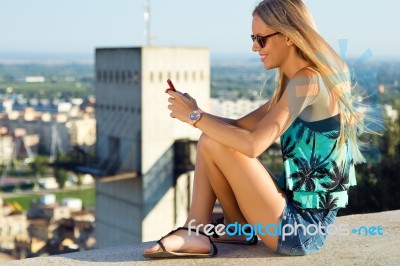 Beautiful Blonde Girl Sitting On The Roof With Mobile Phone Stock Photo