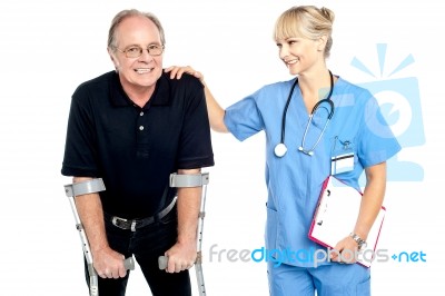 Cheerful Doctor Encouraging Her Patient To Walk With Crutches Stock Photo