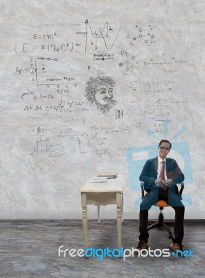 Man Sitting On Desk And Physic Formula On Wall Stock Photo