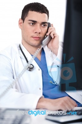 Portrait Of Male Physician Holding Receiver And Looking The Computer Stock Photo