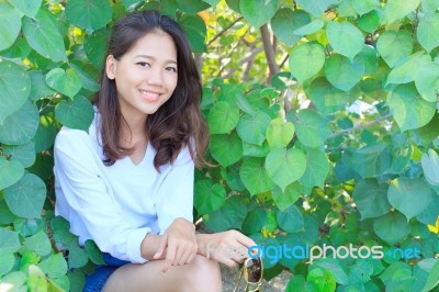 Portrait Of Pretty Woman Sitting In Green Leaves Bush And Smilin… Stock Photo