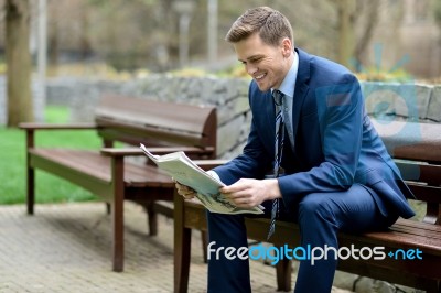Smiling Businessman Reading Newspapers In Park Stock Photo