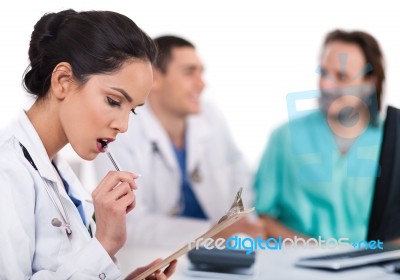 Young Asian Doctor Thinking With The Pen, Others Blurred Behind Stock Photo