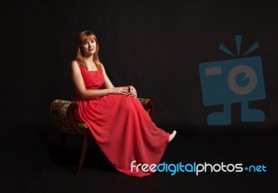 Young Woman In Red Dress Sitting On A Chair Stock Photo