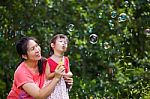 Asian Lovely Girl And Her Mother Blowing Soap Bubbles. Family In Stock Photo