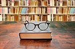 Book With Glasses On The Desk Against Library Stock Photo