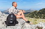 Caucasian Man Sitting With Backpack In Greek Mountains Stock Photo