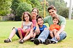 Family Seated In Park And Smiling At Camera Stock Photo