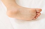 Foot Of Asian Baby On White Bedcovers Stock Photo