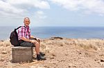 Man With Backpack Sitting Uphill At Sea Coast Stock Photo