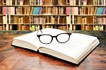 Open Book With Glasses On The Desk Against Library Stock Photo