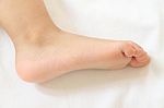 Side Foot Of Asian Baby On White Bedcovers Stock Photo