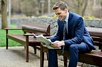 Smiling Businessman Reading Newspapers In Park Stock Photo