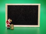 Miniature Santa Claus In Front Of A Blackboard On Green Backgrou Stock Photo