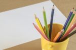 A Lots Of Colour Pencil In Yellow Cup And White Paper On Backgro Stock Photo