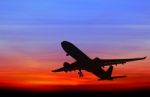 Silhouetted Commercial Airplane Flying At Sunset Stock Photo