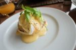 Eggs Benedict Consists Of An English Muffin Topped With Ham Or Bacon, A Poached Egg And Hollandaise Sauce On A White Plate Stock Photo