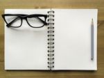 White Paper Note Book With Grey Pencil And Black Glasses On Wood Stock Photo