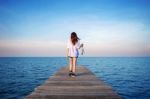 Woman Walking On Wooden Bridge Extended Into The Sea Stock Photo