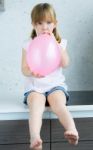 Cute Little  Girl Inflating A Pink Balloon In The Kitchen Stock Photo