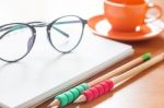 Pencils And Eyeglasses On Open Blank White Notebook With Coffee Stock Photo