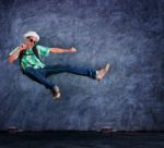 Traveling Man Jumping Mid Air With Exciting Emotion Against Cement Wall Stock Photo