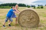 Mother And Son Rolling Hay Bale In Countryside Stock Photo