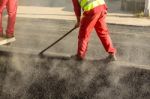 Construction Worker Leveling Fresh Asphalt Pavement During Road Repair Stock Photo