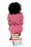 Girl Sitting On Pile Of Books Facing The Wall Stock Photo
