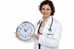 Pretty Doctor Pointing Out Time On Wall Clock Stock Photo