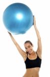 Woman Holding Big Blue Pilates Ball Above Her Head Stock Photo