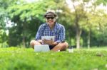 Full Length Of A Happy Smiling Mid Aged Man Sitting In Park Hold Stock Photo