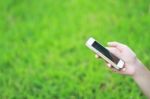 Hand Hold Smart Phone Against Green Grass Background Stock Photo