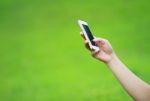 Hand Holding Smart Phone Against Green Grass Background Stock Photo