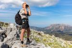 European Man On Rocks Looking Through Binoculars Stock Photo