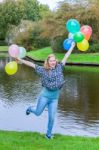 Girl Holding Up Many  Coloured Balloons At Pond Stock Photo