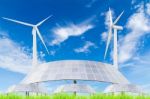 Solar Panels And Wind Turbine On Green Grass Field Against Blue Stock Photo
