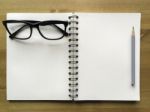White Paper Note Book With Grey Pencil And Black Glasses On Wood Stock Photo