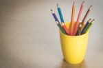 A Lots Of Colour Pencils In Yellow Cup On Wooden Texture Paper Stock Photo
