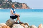 European Woman As Tourist Sitting On Rocks Near Blue Sea Stock Photo