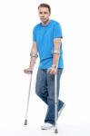 Painful Expression By Young Man Walking With Help Of Crutches Stock Photo