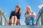 Two Girls Sitting On Metal Bridge With Blue Sky Stock Photo