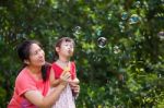 Asian Lovely Girl And Her Mother Blowing Soap Bubbles. Family In Stock Photo