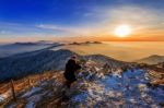 Professional Photographer Takes Photos With Camera On Tripod On Rocky Peak At Sunset Stock Photo